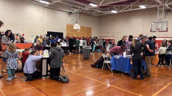 An elementary school gymnasium set up for science night with displays on tables and people mingling