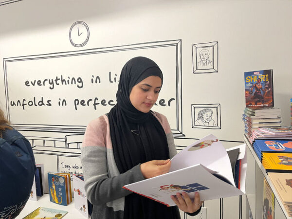 A woman wearing a Hijab reads a book in a library.